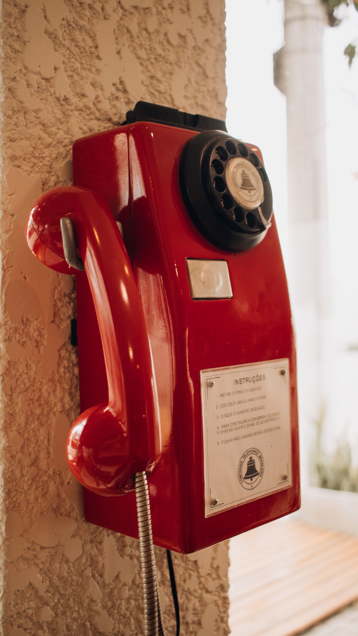 Telefone de parede vermelho com placa de instruções em português